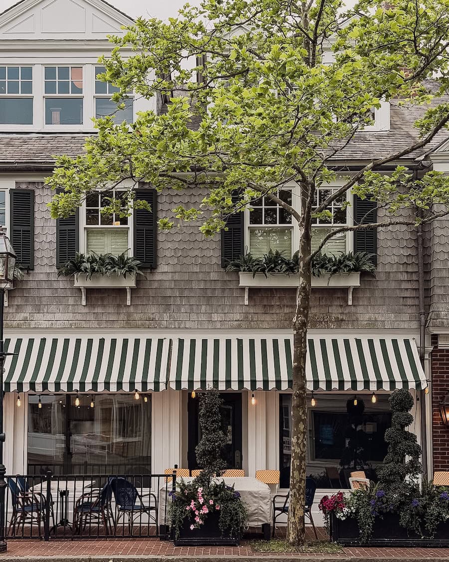 A shingled Martha's Vineyard storefront with a green-and-white awning, cafe tables, and flower boxes